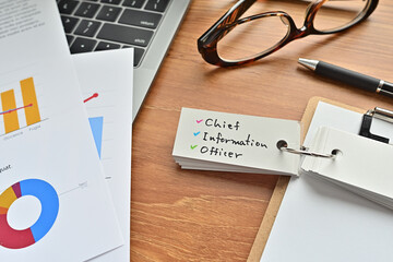 There is a piece of paper with a graph printed on it, a clipboard, and an open vocabulary book on the desk. There is the word chief information officer on it.