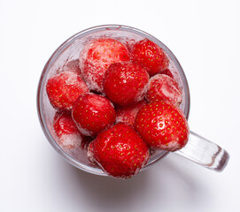 freshly frozen strawberries in a glass mug on a white background.