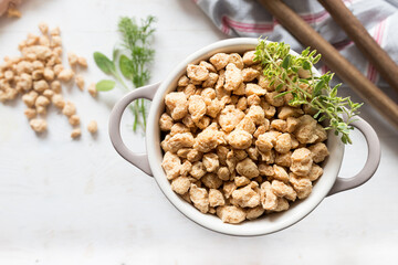 Closeup view of a white casserole full of raw chunks of soya meat. An aromatic twig is at the top.