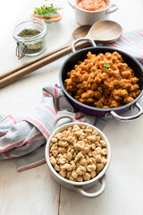 Closeup view of a little white casserole full of soya raw chunks. A casserole of bolognese soya meat is as background.
