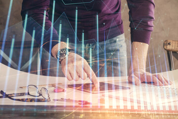 Double exposure of man's hands holding and using a digital device and forex graph drawing. Financial market concept.