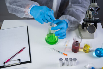 Technician in protective clothing hand stirring and shaking green liquid in Erlenmeyer flask in chemical laboratory. Laboratory technician studies chemical reactions and searches for cancer drug