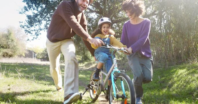 Girl learning to ride a bike with parents help outdoors