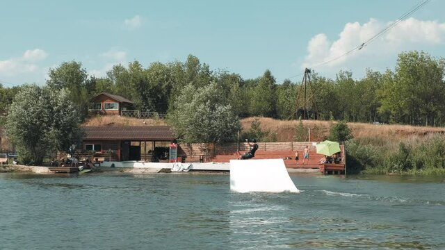 Full shot of professional surfer on wakeboard performing backside lipslide in lake holding wakeboard rope