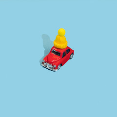 Red toy car in yellow winter cap on blue background. Minimal Happy New Year concept