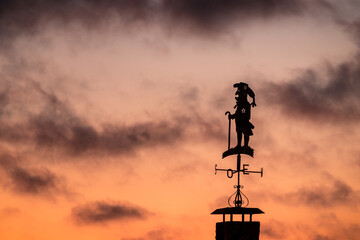 Wind vane in the shape of a cane man, silhouetted against a sunset sky.