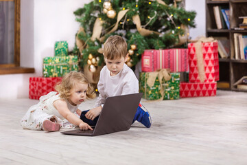 Young girl and boy watching video on laptop computer beside Christmas tree