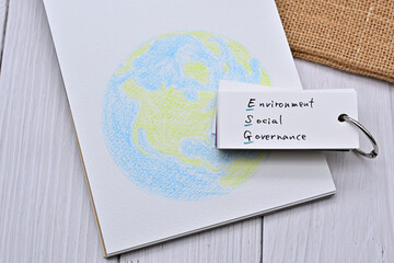 A wordbook with the word "Environment Social Governance" written on it sits beside a sketchbook with an illustration of the Earth.