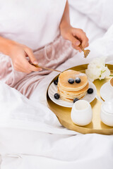 Obraz na płótnie Canvas Cropped view of cutlery in hands of woman near pancakes with berries on bed on blurred 