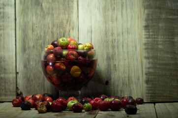 Cup with Acerola fruits (Malpighia emarginata) on wooden background in selective focus