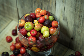 Cup with Acerola fruits (Malpighia emarginata) on wooden background in selective focus