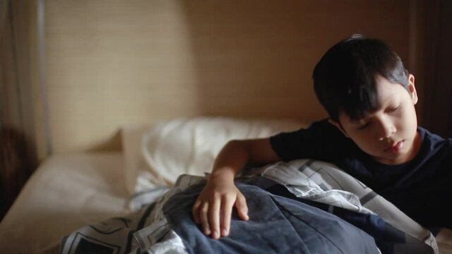 Asian child boy wake up scratching the head then looking the alarm clock and shocked as he wake up late to go to school. Boy on bed in bedroom at home. Kid waking up from sleep in the morning