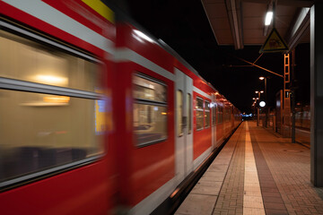 Obraz premium Night scenery at empty platform of train station without people and blurry movement of religion train in Germany.