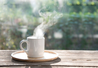cup of coffee with smoke on wooden table and green blur background in the morning