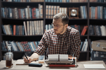 A young writer with glasses sitting at a Desk writes a story with a fountain pen next to a...