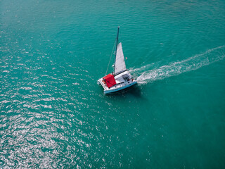 Sailing ship yachts with white sails and  red awning from the sun for passengers at open sea. Aerial - drone view to sailboat in windy condition