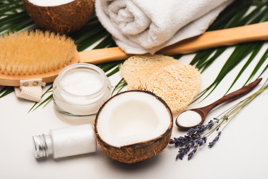 coconut half, cosmetic cream, massage towel, sponges and palm leaves on white surface, stock image