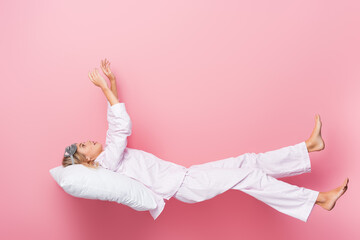  woman in pajamas lying on pillow on pink background