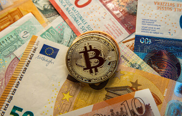 Shiny Bitcoin coins lying on European banknotes - Czech crowns, Swiss francs, British pounds.