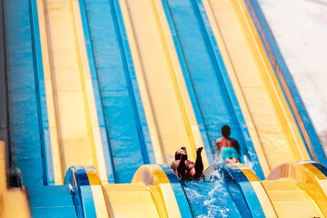 Cool people having fun on the water slide with friends and familiy in the aqua fun park glides playing happy and water splashes are all over. Aqua fun park glides playing happy in the sunlight sky