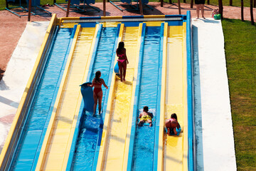 Cool people having fun on the water slide with friends and familiy in the aqua fun park glides playing happy and water splashes are all over. Aqua fun park glides playing happy in the sunlight sky