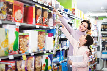 Fototapeta premium Young woman customer with girl looking for breakfast cereal in supermarket. Focus on both persons