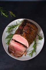 Roasted beef with herbs on dark background. View from above, top studio shot