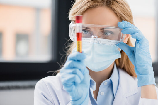 scientist in goggles, latex gloves and medical mask holding test tube with covid lettering, stock image