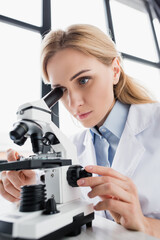  scientist looking through microscope on blurred foreground