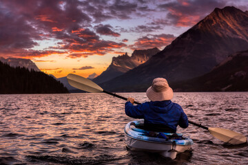 Adventurous Man Kayaking in Glacier Lake surrounded by the beautiful Canadian Rocky Mountains during a cloudy summer sunset. Taken in Upper Waterton Lake, Alberta, Canada.