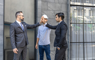 Three senior business men or engineers stand to support each other in front of their office. Team work and cooperation across diverse ethnicities.