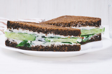 sandwich with black bread, cucumber and cream cheese on a plate on white background. vegetarian food concept