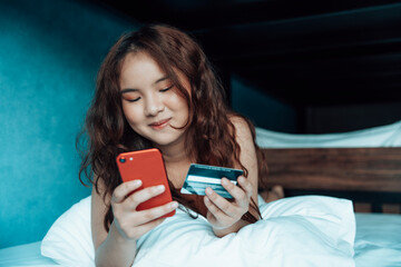 Asian woman using credit card for online shopping in bedroom.