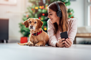 A teenage girl listens to music while lying on the floor with her dog near the Christmas tree