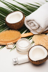 Fototapeta na wymiar coconut halves, homemade cosmetic cream and lotion near towel, massage brush, and palm leaves on white, stock image