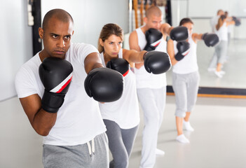 Portrait of confident hispanic male wearing boxing gloves in group workout time in self-defense in gym