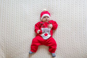Closeup portrait of newborn baby. Cute Caucasian baby girl 3-4 months old in Santa costume lying on knitted cozy blanket on bed. Merry Christmas xmas and happy new year 2021