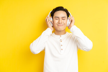 Photo of Asian man in white shirt listening to music with his eyes closed on yellow background