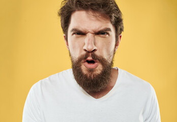 A man with a beard and mustache on a yellow background and a white T-shirt