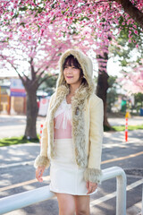 Obraz premium Happy young girl in a wool sweateron is enjoy and relax on a background with sakura cherry blossoms tree on vacation while spring in asian. Travel concept