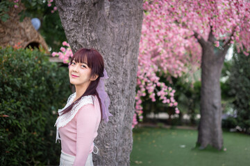 Happy young girl in a pink shirt is enjoy and relax on a background with sakura cherry blossoms tree on vacation while spring in asian. Travel concept