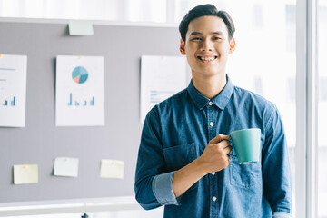 Asian man holding coffee cup standing smiling with planning board background