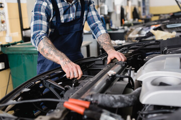 cropped view of mechanic checking car engine compartment in workshop on blurred 