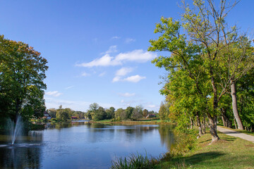 Fototapeta premium Lake Jaunpils on a clear sunny day. Walking path in park along the pond.