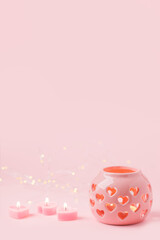 Decorative pink ceramic lanterns with heart cutouts lit by glowing candles onpink background, copy space, Saint Valentine, Mother day, Woman day concept, vertical flyer, greeting card, invitation