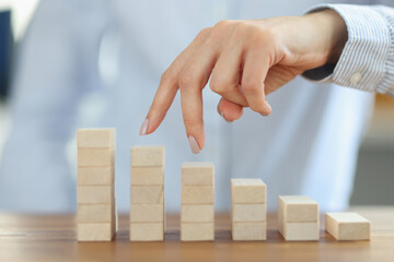 Womans fingers are walking up stairs made of wooden blocks closeup. Business career development concept
