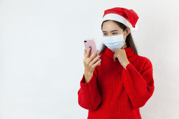 Fototapeta na wymiar asia woman in a Santa hat in a protective mask, in a red sweater,holding mobile phone on white background