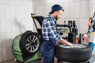 repairman in overalls putting wheel on tire changing machine in workshop, stock image