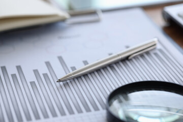 Ballpoint pen and magnifying glass lying on documents with graph in office closeup. Dynamics of...