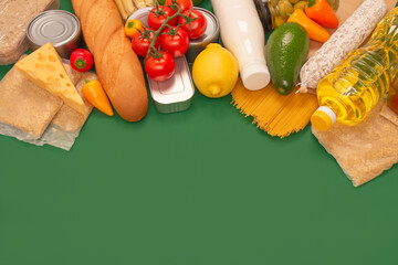 Different groceries or food donations on green background with copyspace - pasta, fresh vegatables, canned food, baguette, cooking oil, tomatoes, cheese. Food bank or food delivery concept